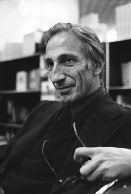 photo of Illich holding his glasses seated in front of a bookcase