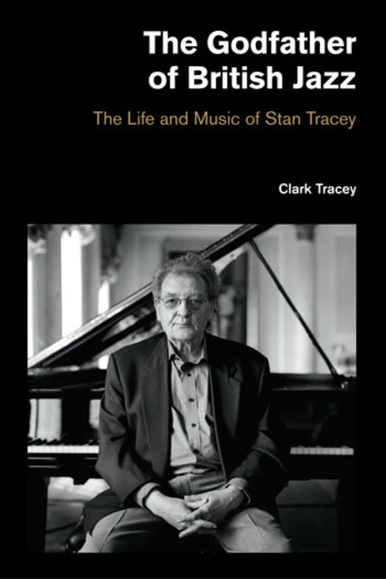 photo of Tracey sitting, facing out, on piano stool in front of a grand piano