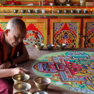 monk seated at a table working on a mandada with coloured sand in bowls
