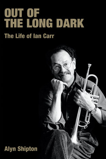 photo of a seated Carr with crossed legs, holding a trumpet 